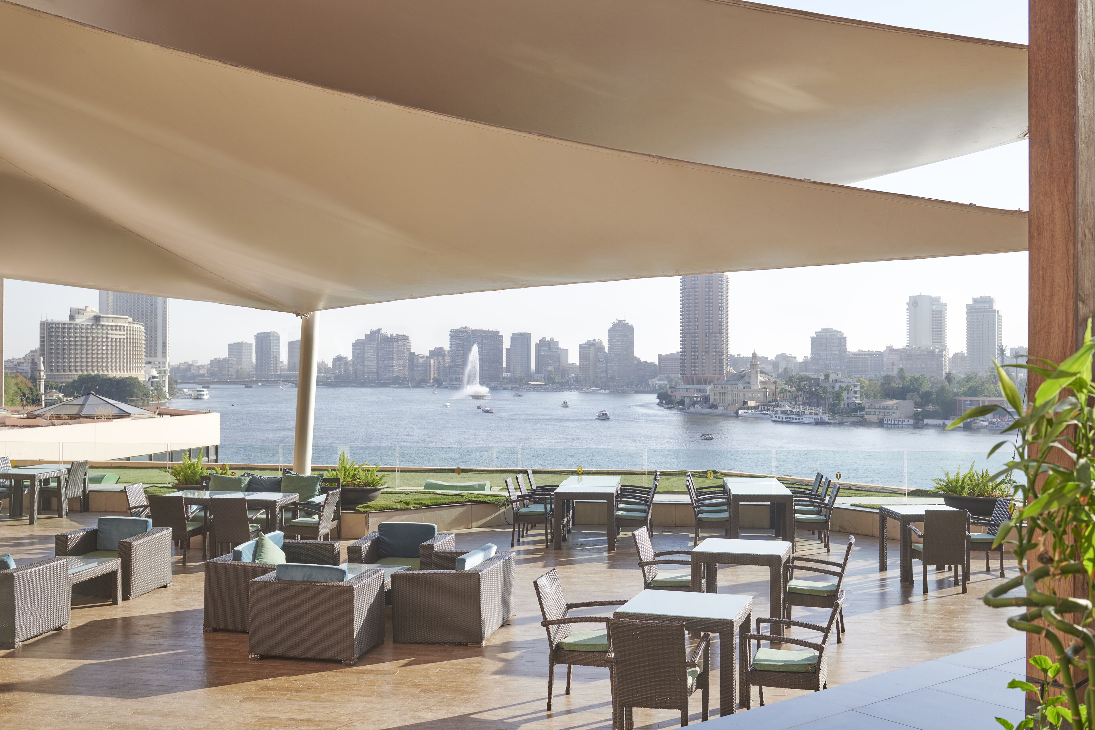An outdoor seating area with tables and chairs, overlooking a body of water and a city skyline.