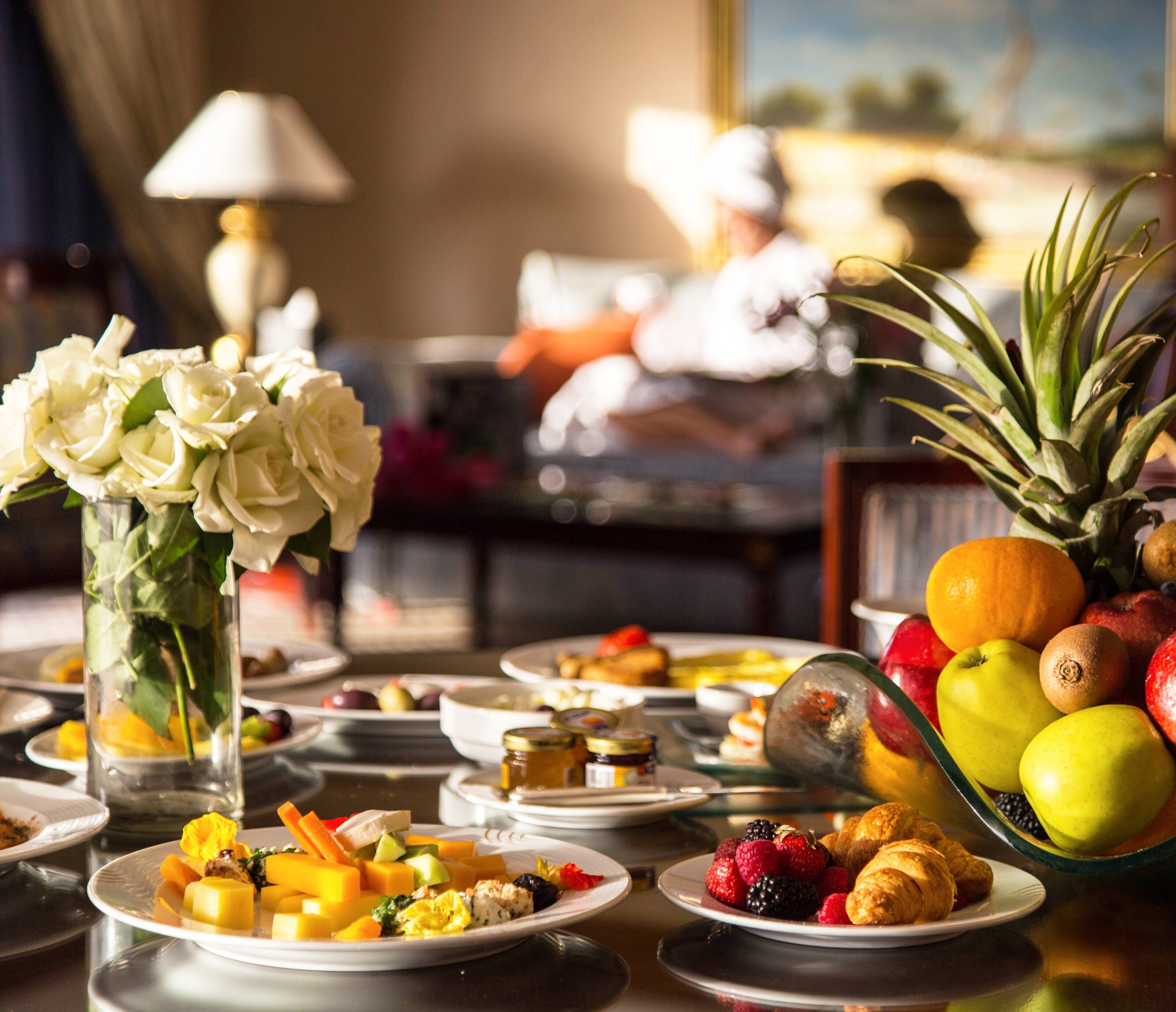 A breakfast setting with a variety of fruits, pastries, and a vase of white flowers on a table.