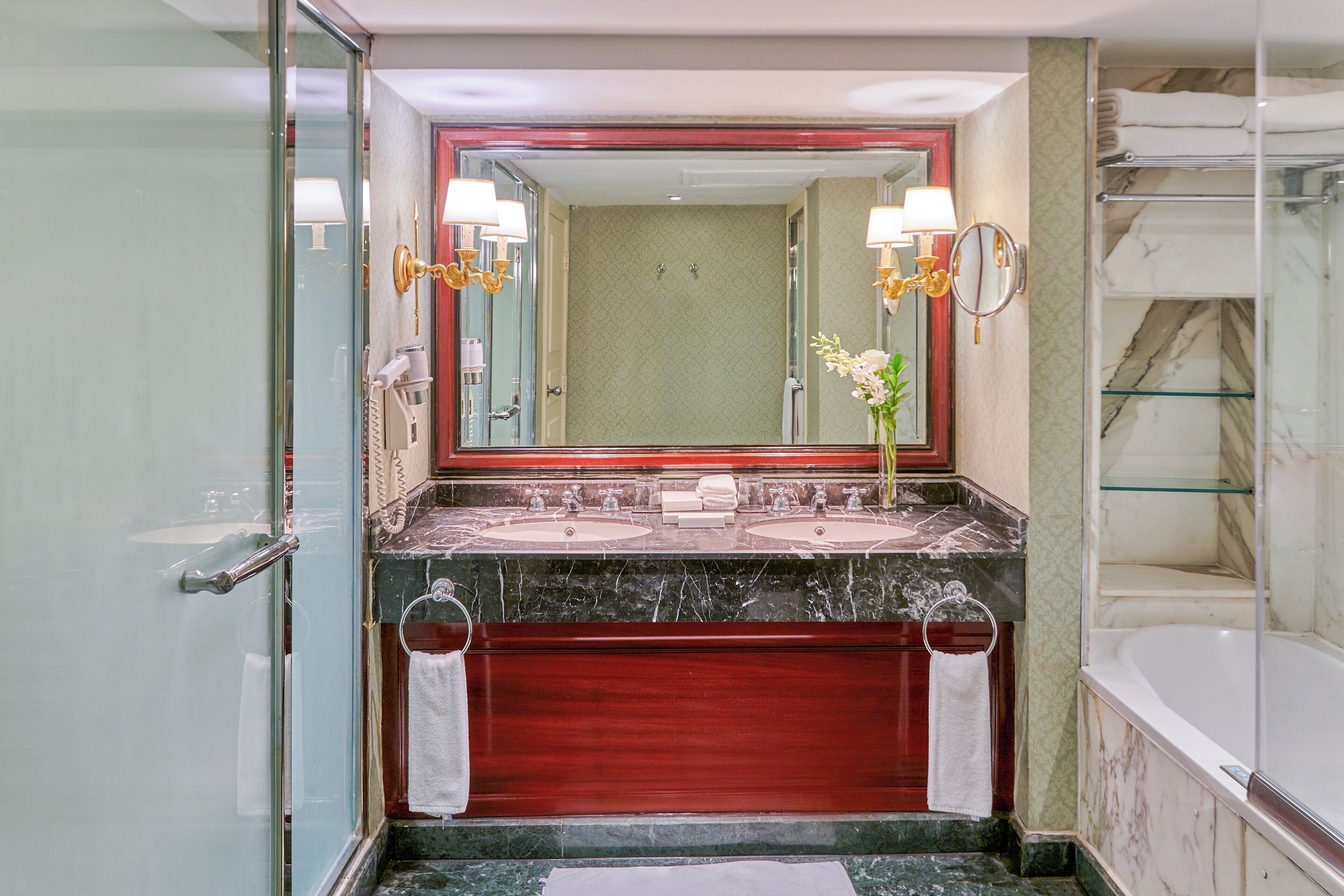 Une salle de bain dotée d’un grand miroir, de deux lavabos, d’une baignoire et d’une douche à parois de verre.
