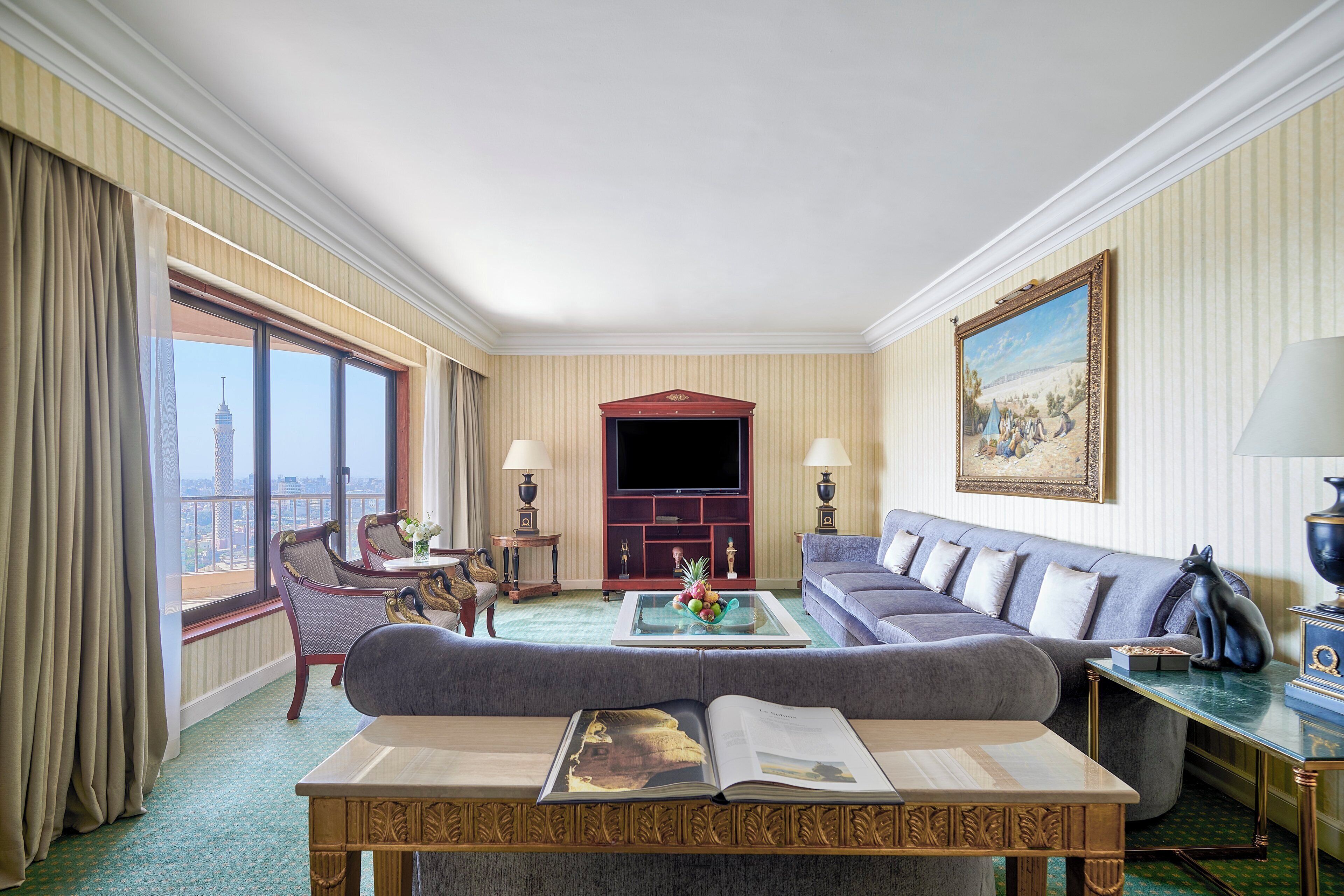 Ein Hotelzimmer mit großem Fenster, einer Couch, einem Couchtisch mit einem Buch und einem Fernseher.