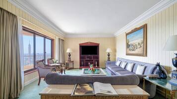 A hotel room with a large window, a sofa, a coffee table with a book, and a television.