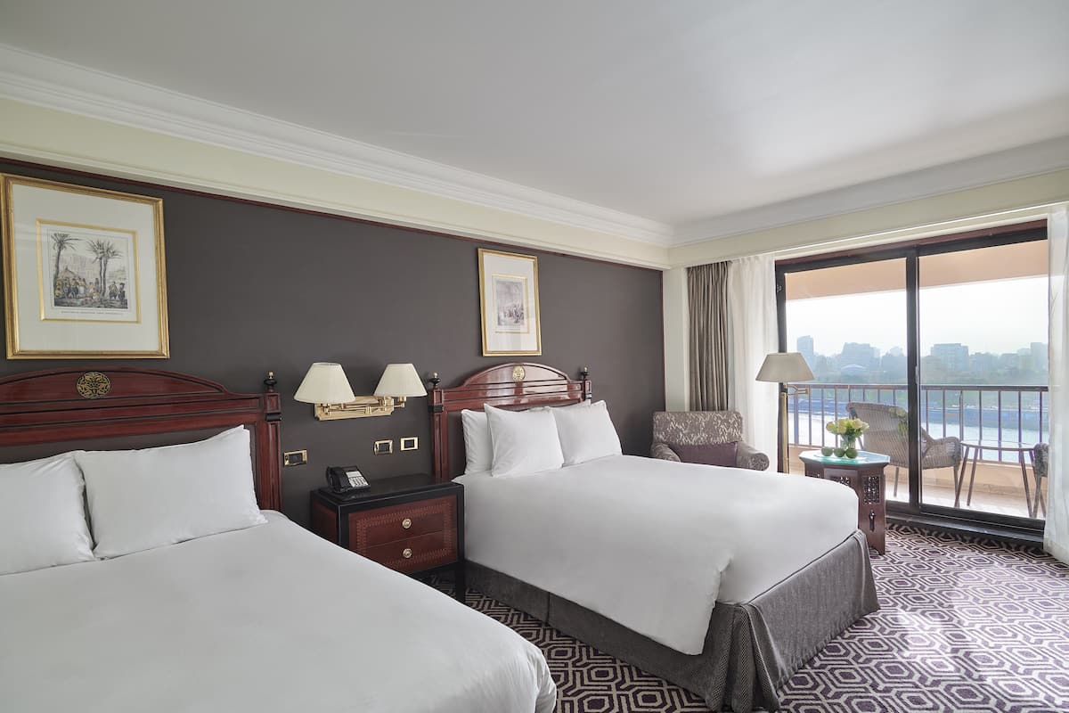 A hotel room with two beds, a balcony with a view, and a cityscape in the background.