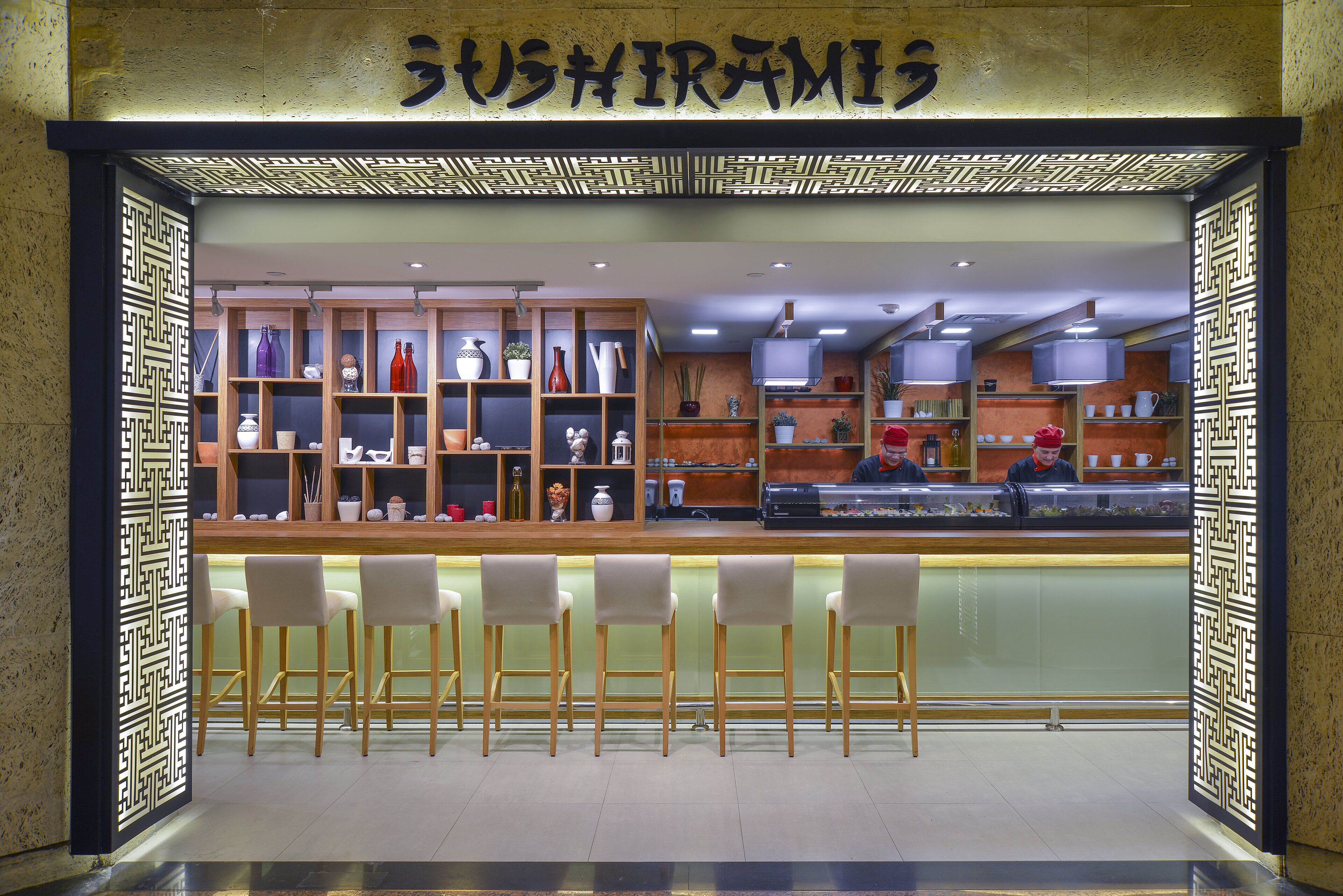 A sushi restaurant with a counter, bar stools, and shelves of dishes and utensils.