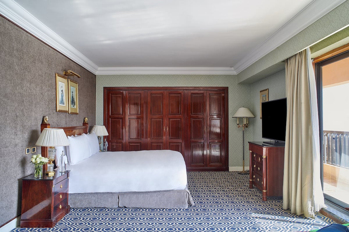 A hotel room with a large bed, wooden wardrobe, a television, and a patterned floor.