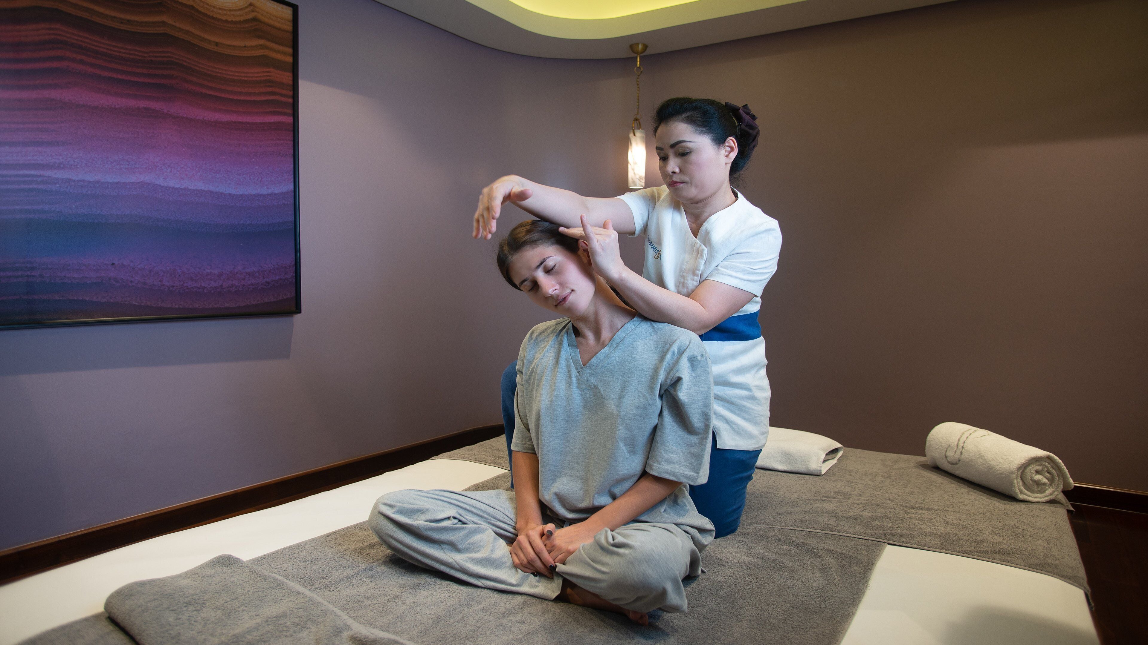 A massage therapy session in a room with a large abstract painting, a wooden floor, and a massage table.