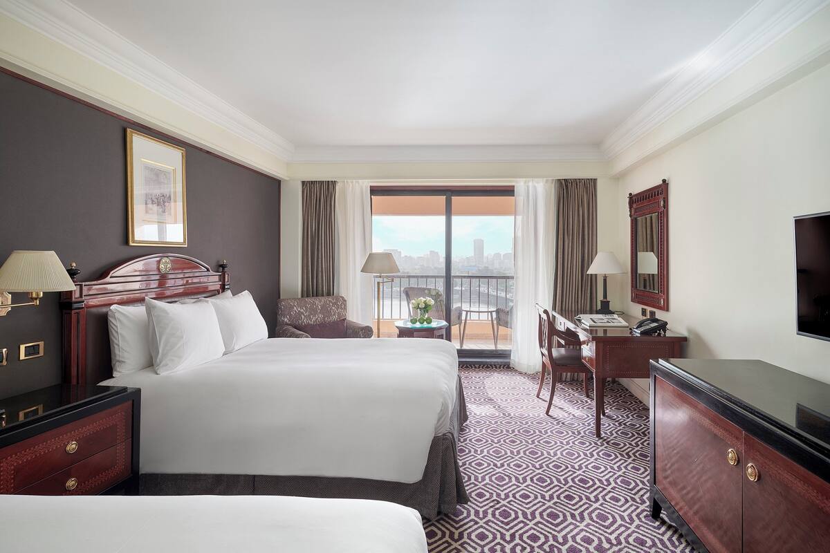A hotel room with a large bed, a desk, a chair, a television, and a balcony with a city view.