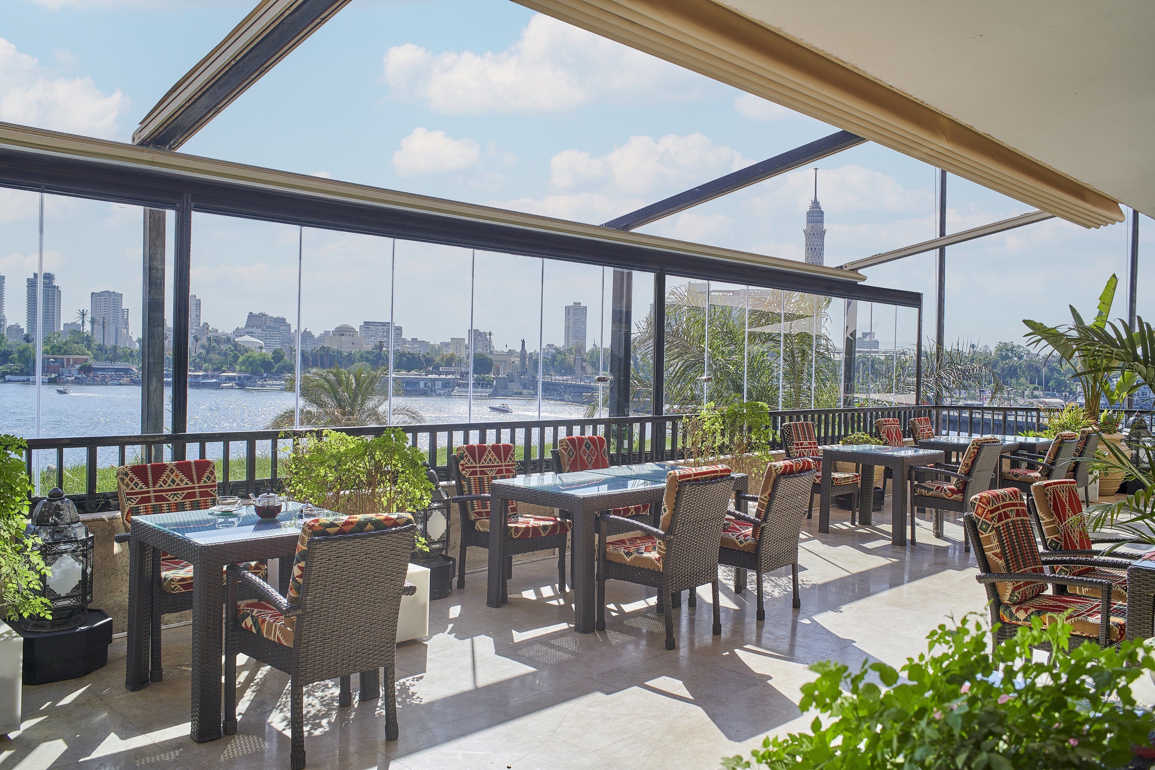 A terrace with outdoor seating, large windows, and a view of a city skyline and water.