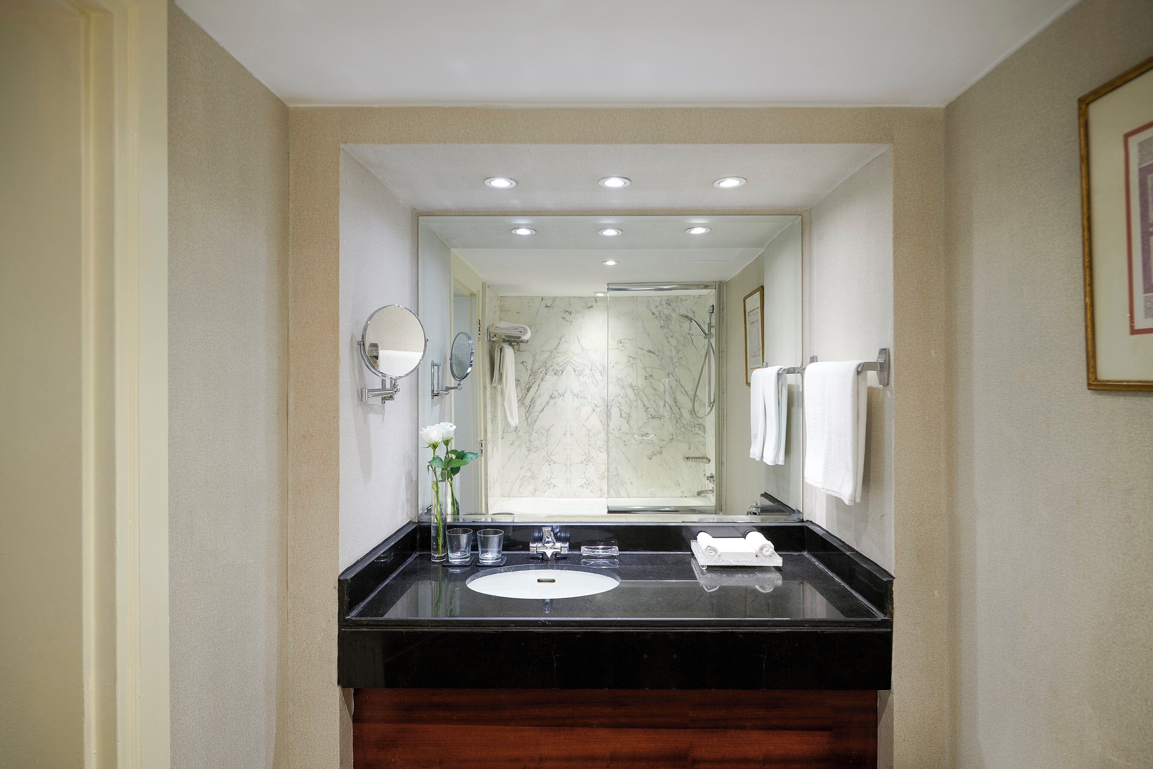 A modern bathroom with a black sink, marble shower, and white towels.
