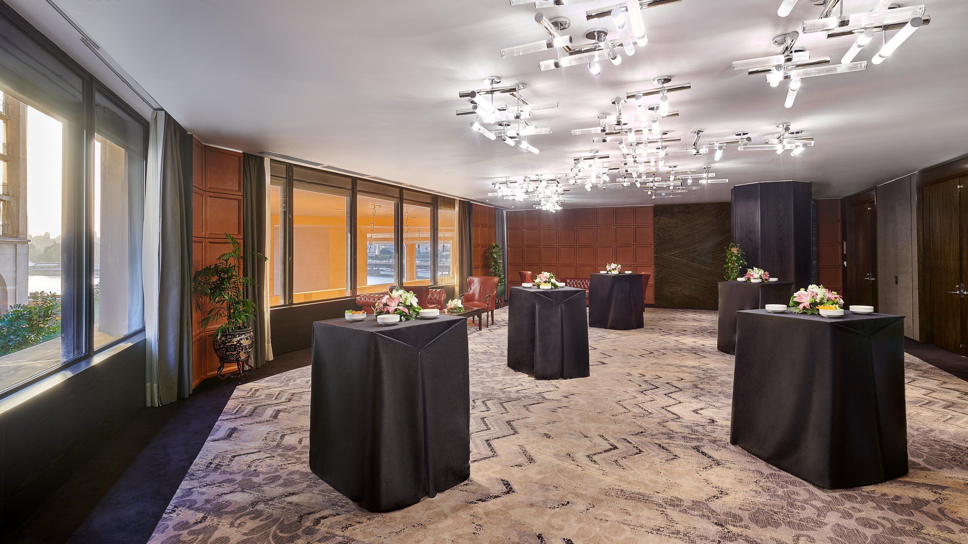 A conference room with multiple tables, a large window with curtains, and a patterned carpet.