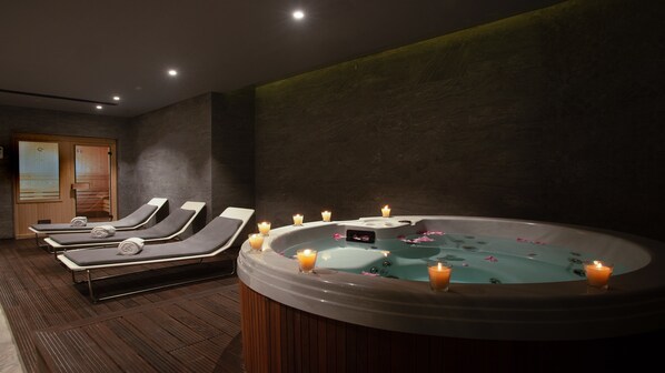 A spa area with a hot tub surrounded by candles, wooden flooring, and lounge chairs.