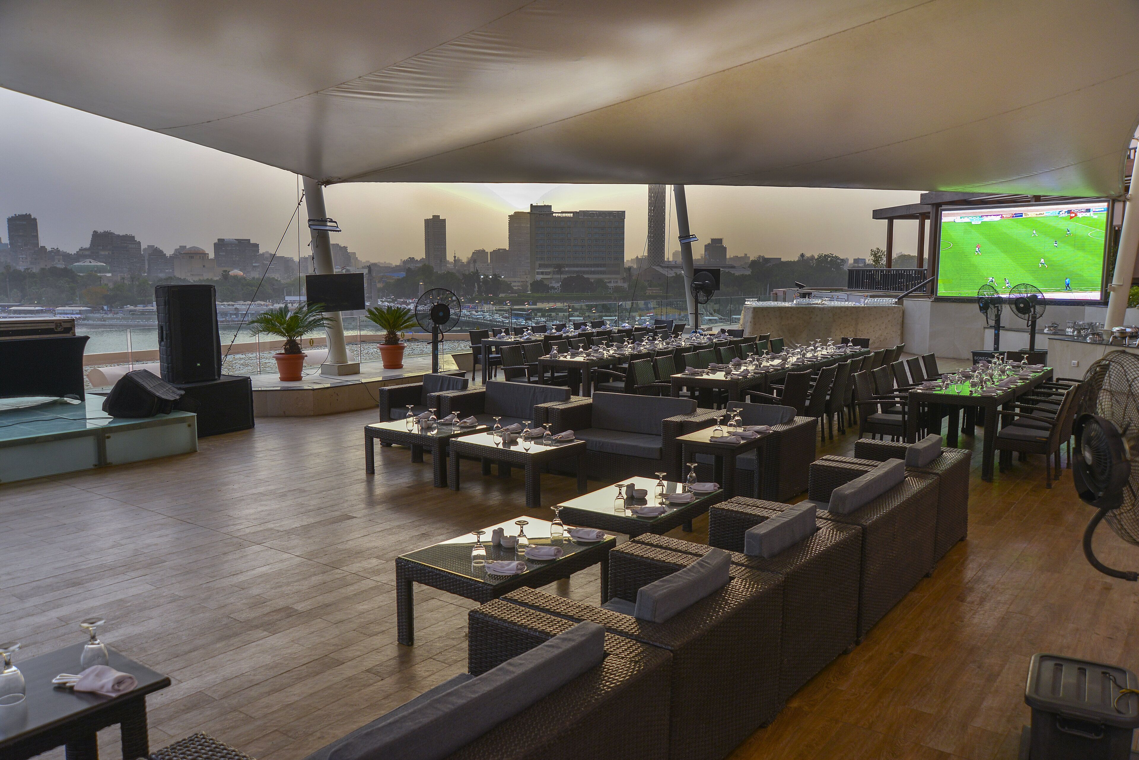 Un bar en la azotea con varias zonas de estar, una pantalla grande para ver deportes y vistas a un horizonte urbano.