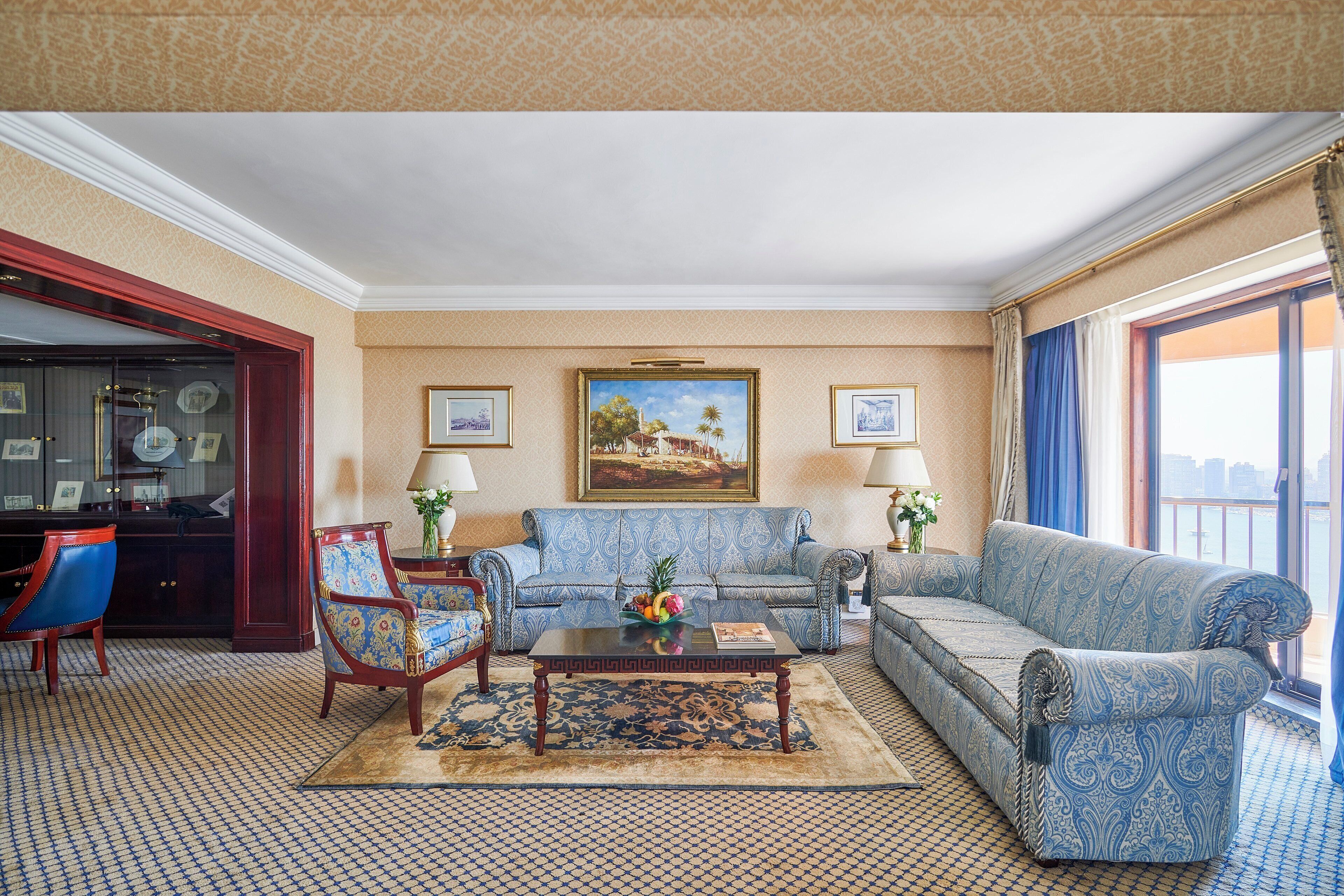 Un salon spacieux avec un tapis à motifs, un ensemble de canapés bleus, une table basse et un bureau avec une lampe.