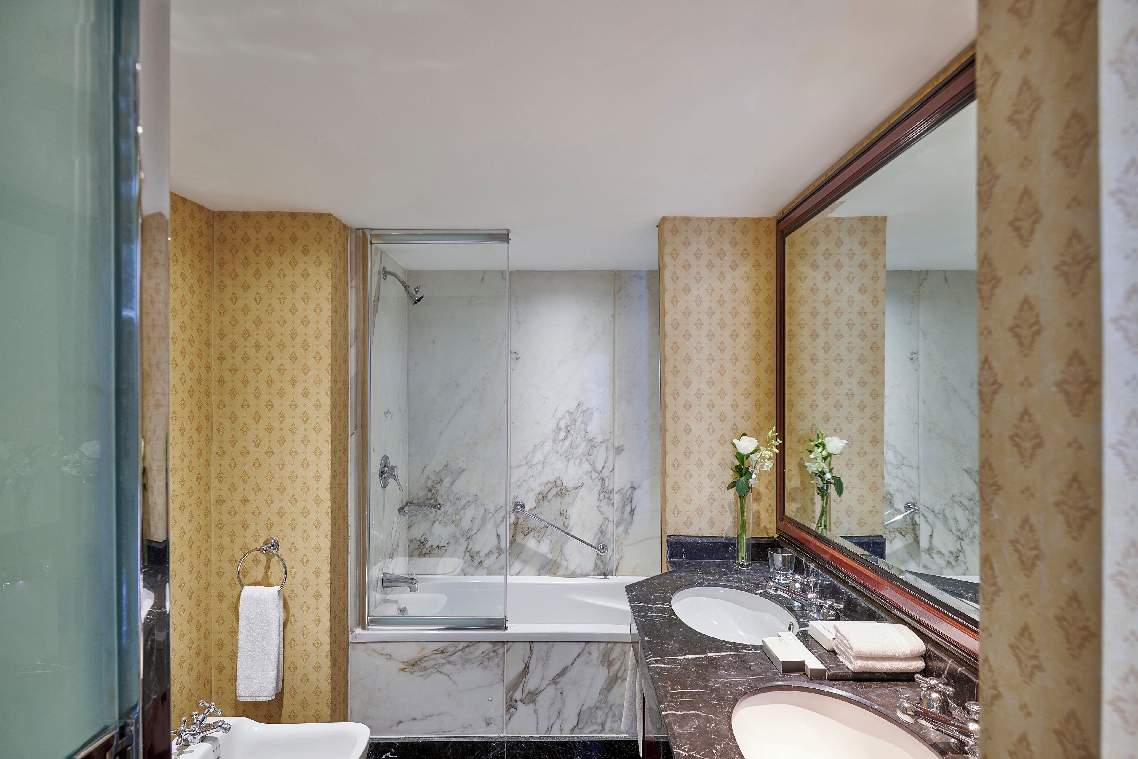 A modern bathroom with a glass-enclosed shower, a marble-tiled wall, a vanity with a sink, and a large mirror.