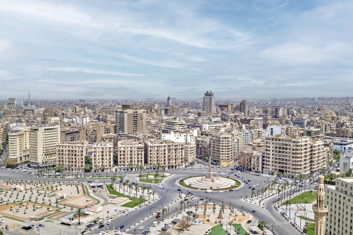 A cityscape with a central roundabout, surrounded by multi-story buildings, and a prominent minaret in the distance.