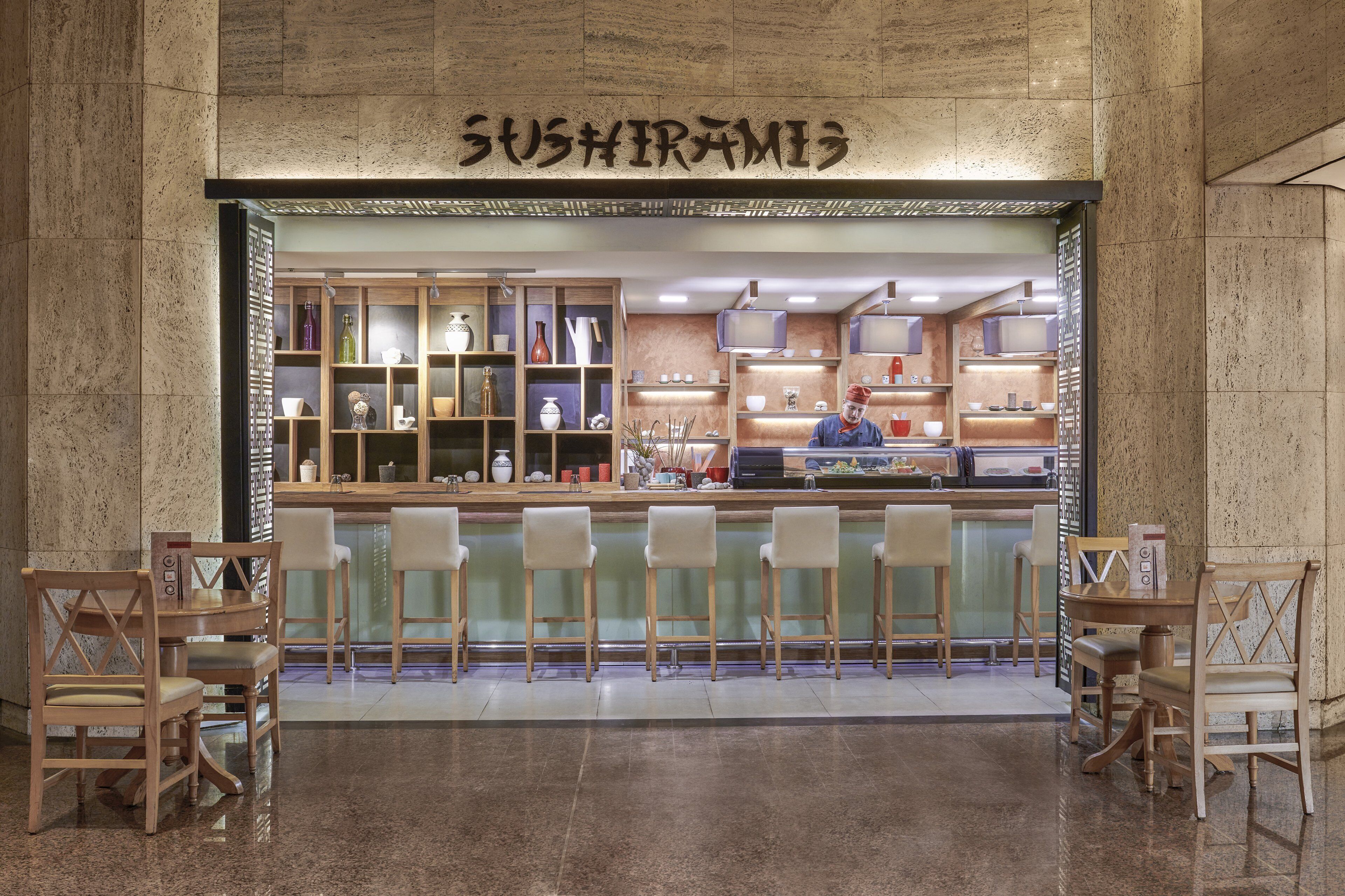 Un restaurante de sushi con barra, taburetes y estantes llenos de vajilla.