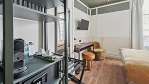 A hotel room with a bed, a desk with a computer, a chair, a small stool, a coffee maker, and a water dispenser. - D'win Hotel (Paris)