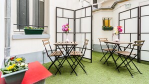 A small outdoor seating area with two tables and four chairs, a potted plant, and a window with a view of the building's exterior. - D'win Hotel (Paris)