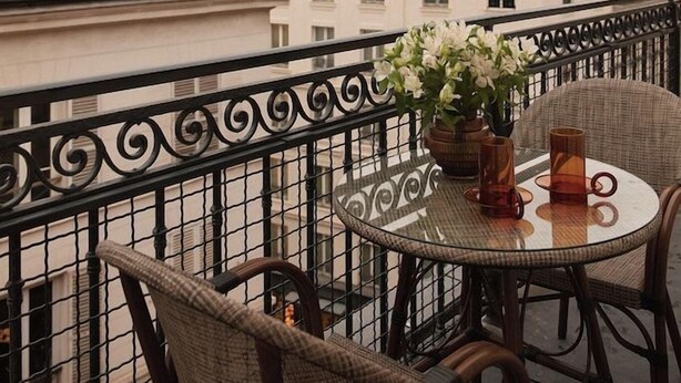 A balcony with wicker chairs and a table, overlooking a row of buildings with multiple windows and a dome-shaped structure. - La Boetie (PARIS)