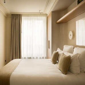 A hotel room with a large bed, a window with curtains, and a wall-mounted light fixture. - La Boetie (PARIS)