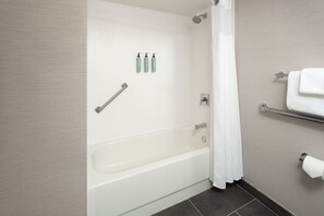 A modern bathroom with a bathtub, a shower curtain, a towel rack, and toiletries on the wall. - Courtyard By Marriott Shelton (Shelton)