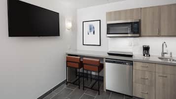 A modern kitchen with a flat-screen TV, a microwave, a coffee maker, and a dishwasher.