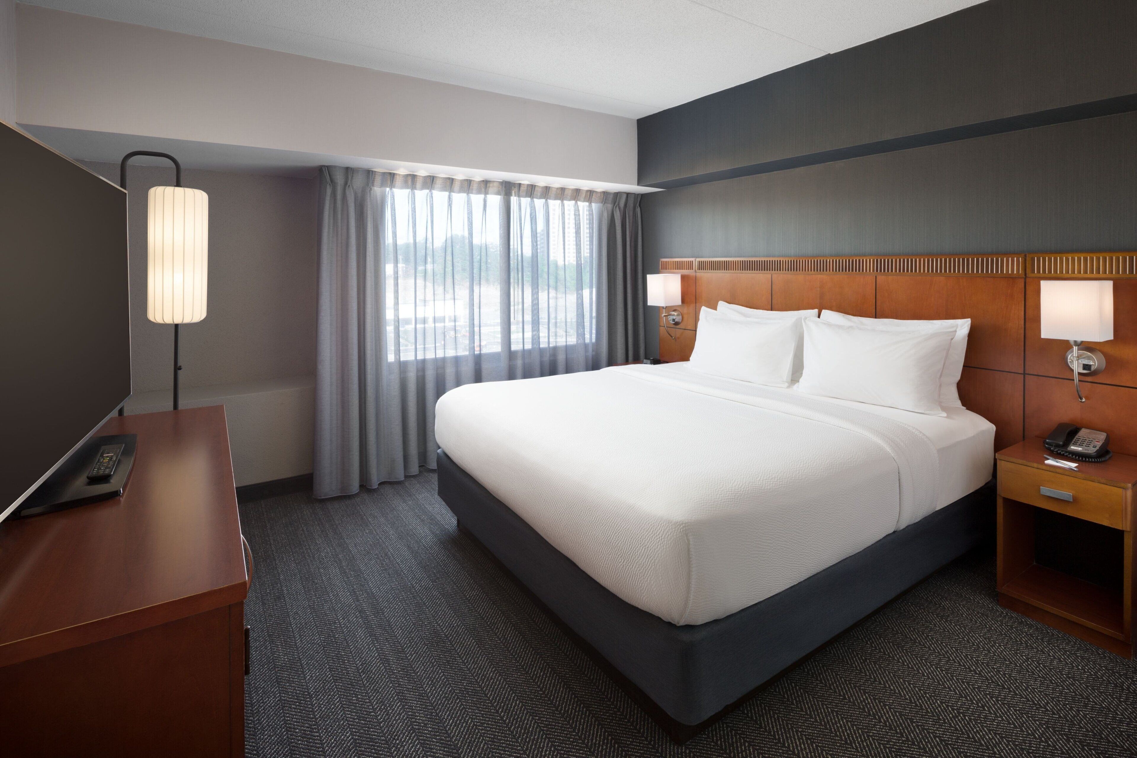 Una habitación de hotel con una cama grande, un escritorio con una lámpara y un teléfono en la mesita de noche.