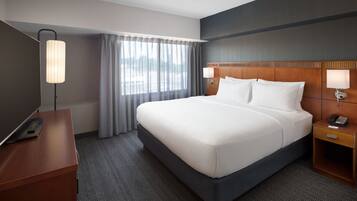 Una habitación de hotel con una cama grande, un escritorio con una lámpara y un teléfono en la mesita de noche.