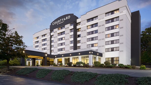 Un hotel de varios pisos con un llamativo letrero de "Courtyard by Marriott", que presenta un diseño arquitectónico moderno con techo plano y amplias ventanas.