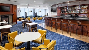 Un vestíbulo de hotel con zona de bar, disposición de asientos y chimenea.