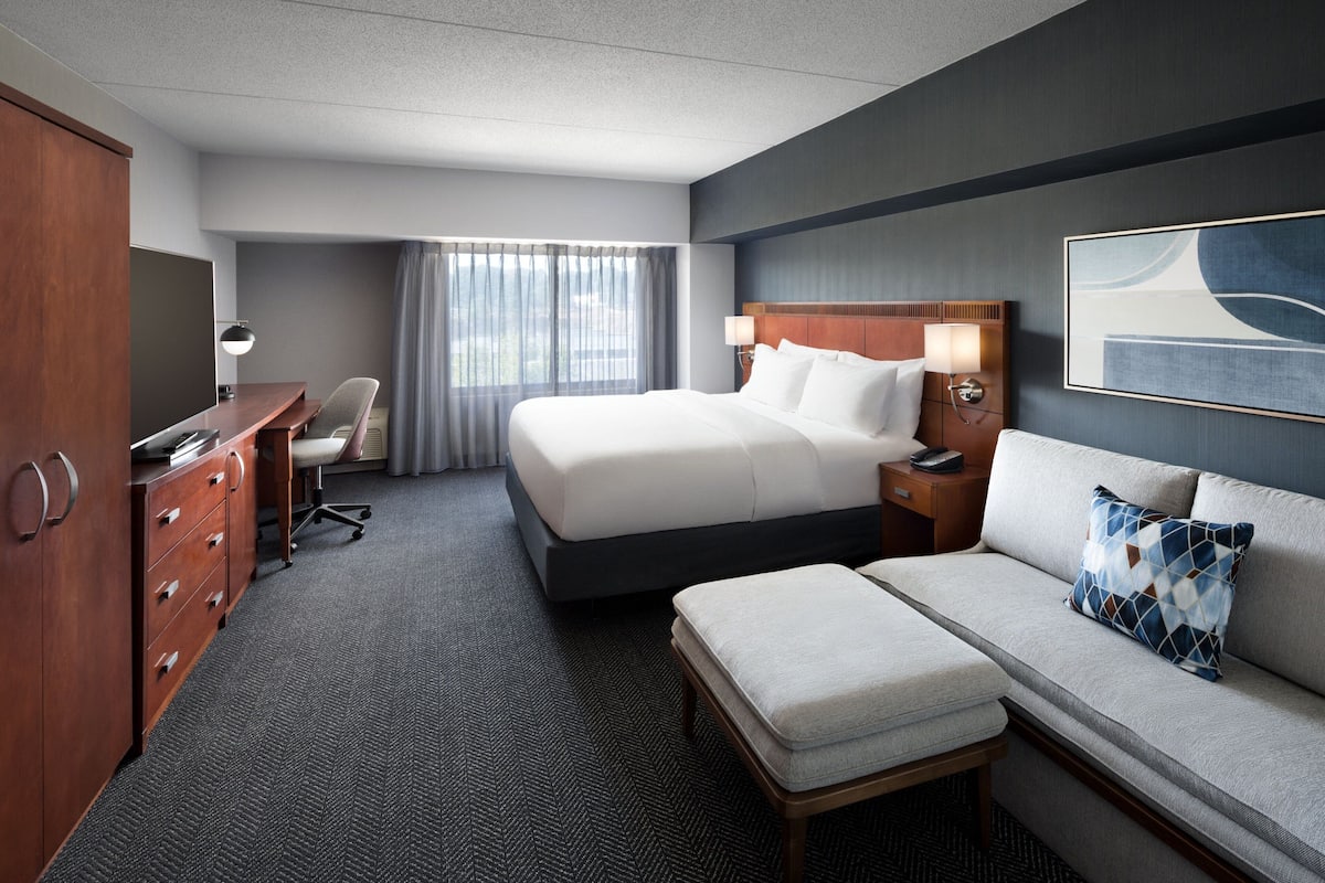 Quarto de hotel com uma cama grande, uma escrivaninha com cadeira, um sofá e um guarda-roupa.