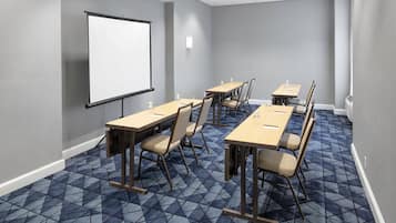 Una sala de conferencias con pantalla para proyector, varias mesas y sillas.