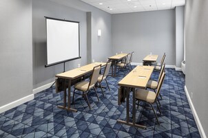 Una sala de conferencias con pantalla para proyector, varias mesas y sillas.