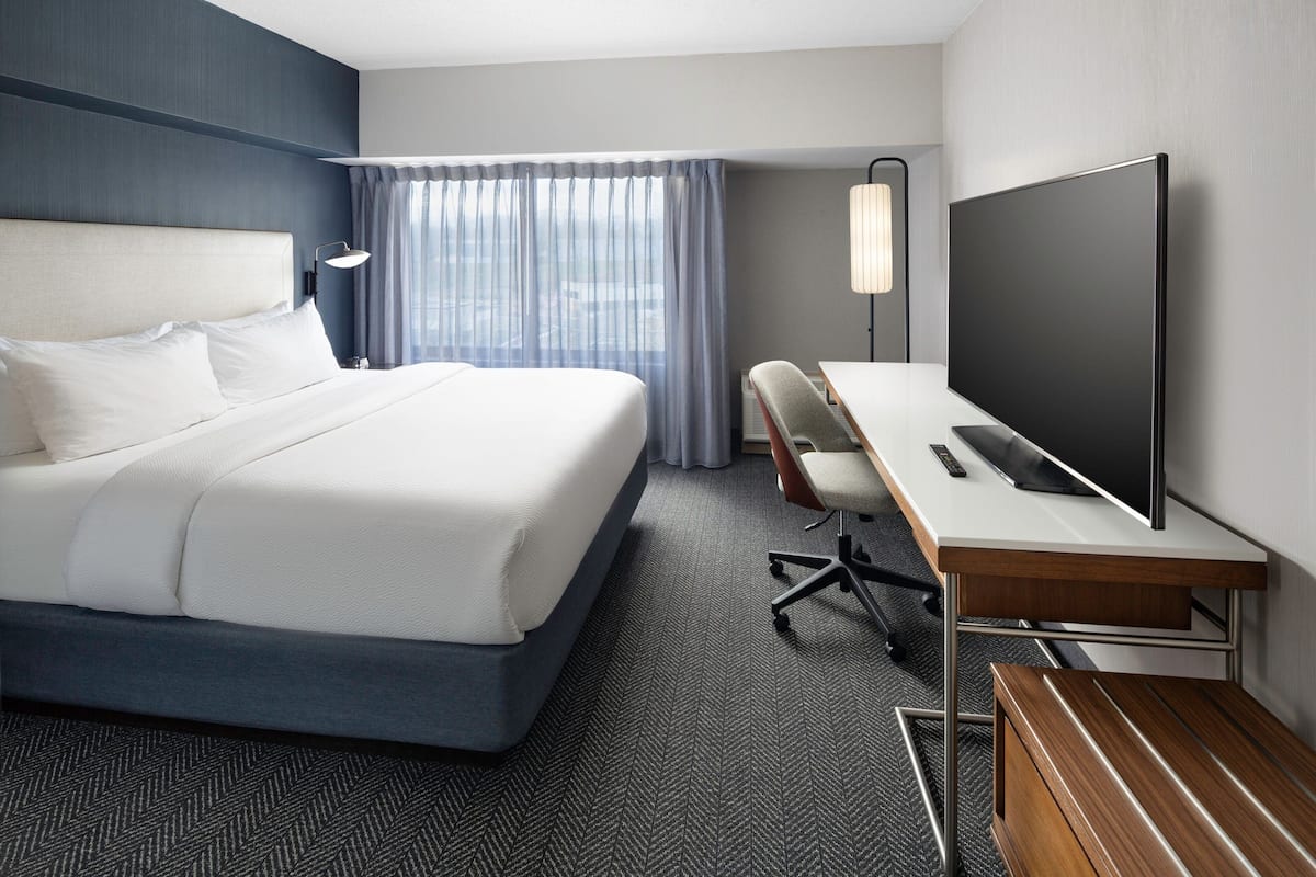 Quarto de hotel com uma cama grande, uma escrivaninha, uma televisão de tela plana, uma cadeira e um abajur.