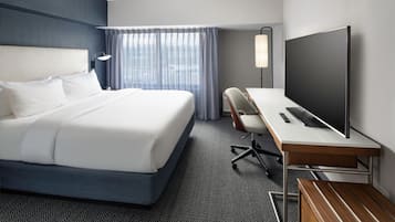 Quarto de hotel com uma cama grande, uma escrivaninha, uma televisão de tela plana, uma cadeira e um abajur.