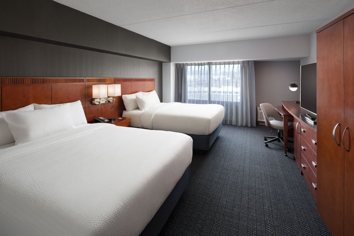 Quarto de hotel com duas camas, uma escrivaninha, uma televisão e um guarda-roupa.