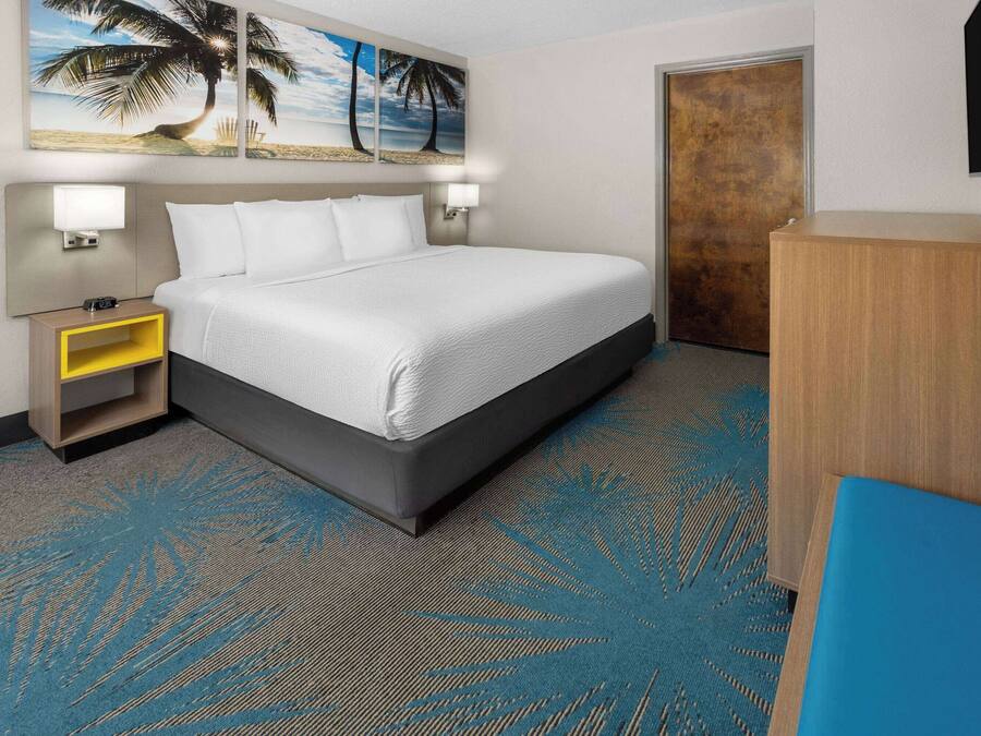 A hotel room with a bed, nightstand, lamp, and a television on the wall.