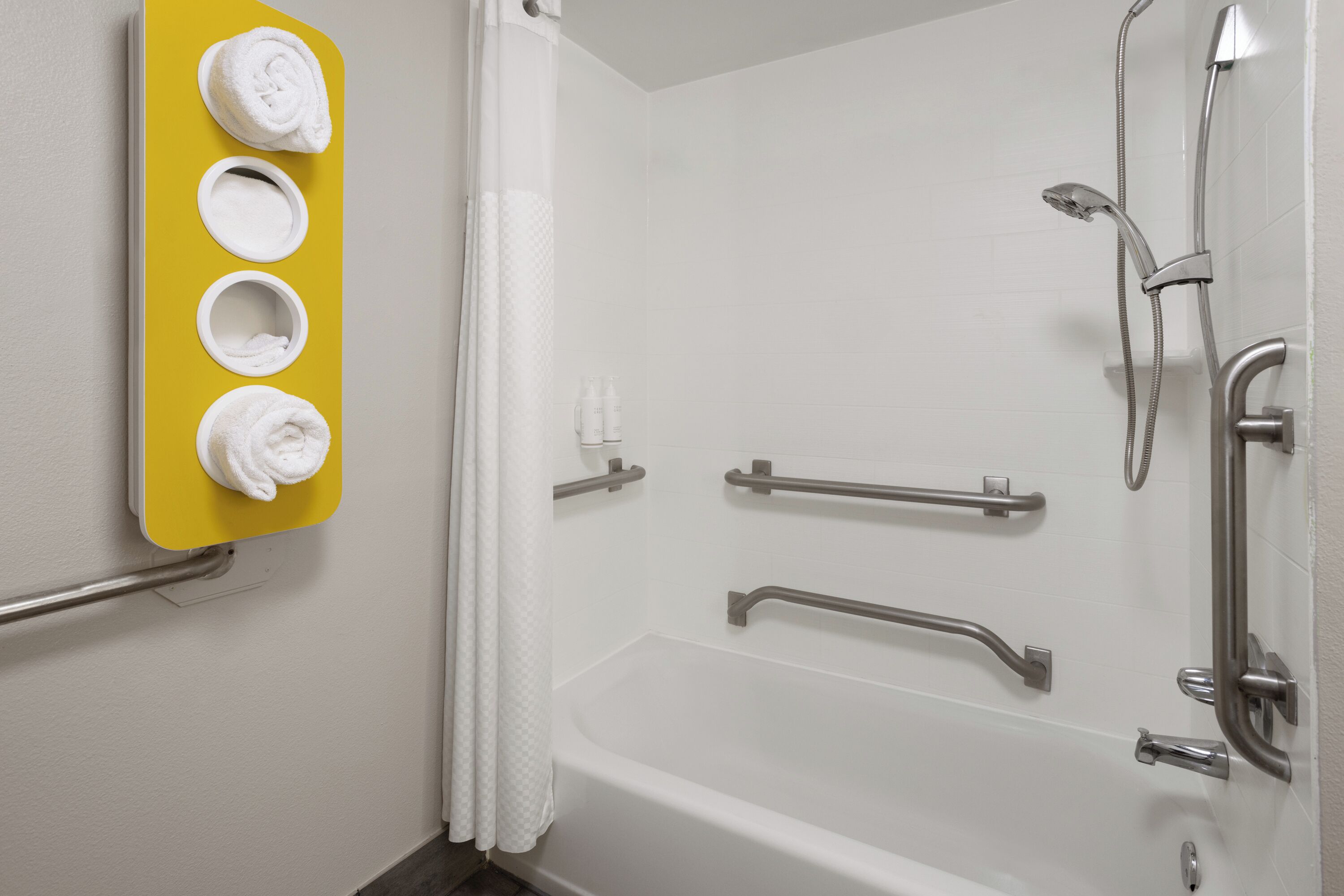 Une salle de bain équipée d’une baignoire, de barres d’appui, d’une douche avec un pommeau de douche amovible et d’un porte-serviettes avec des serviettes.