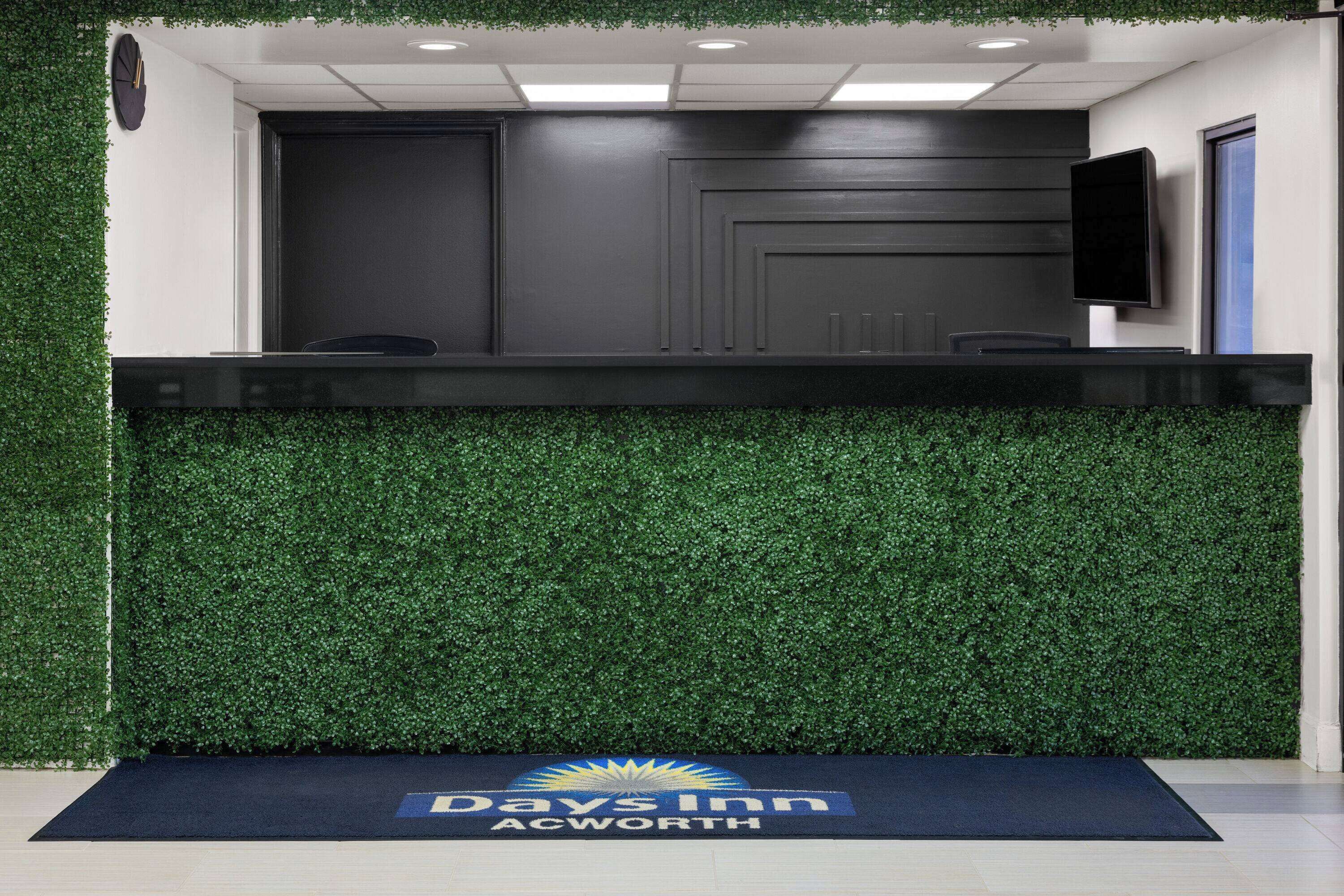 Un espace d’accueil doté d’un comptoir sombre, d’un téléviseur à écran plat et du logo de l’hôtel Days Inn ACWORTH.