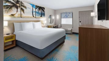 A hotel room with a bed, a desk, a chair, a mirror, a TV, and a bathroom.