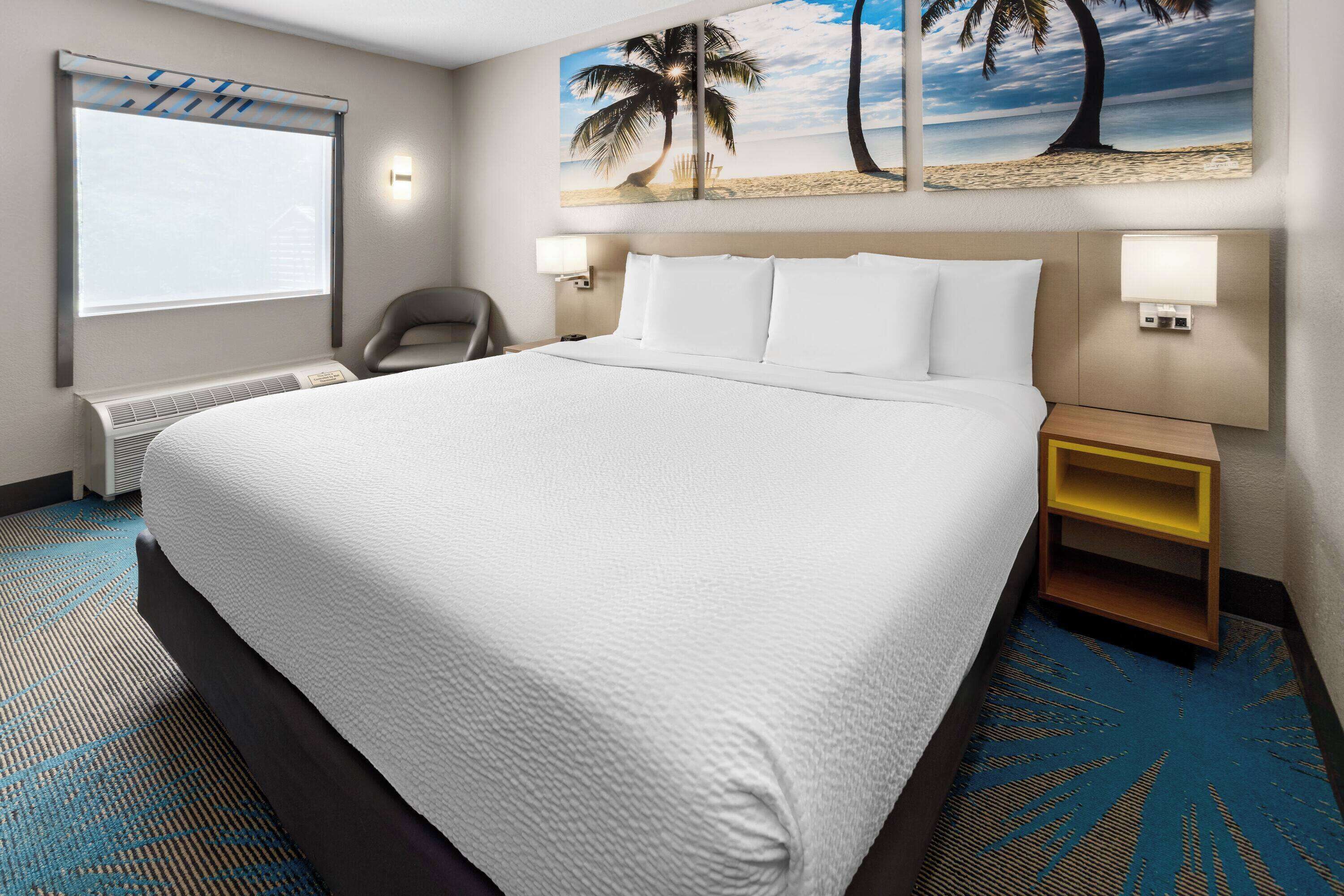 A hotel room with a large bed, a chair, a nightstand, and a wall-mounted lamp.