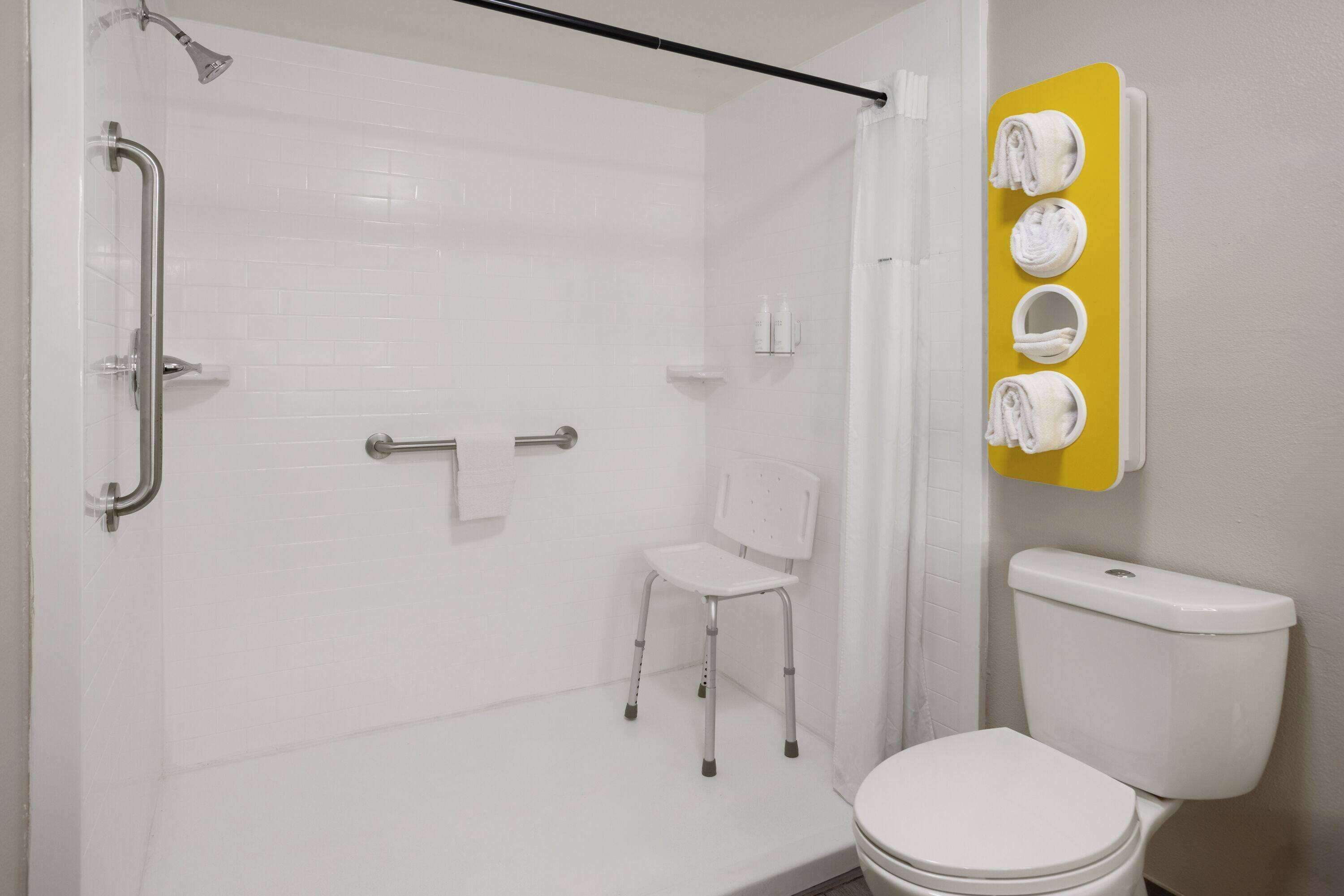 A bathroom with a shower, a toilet, and a chair.