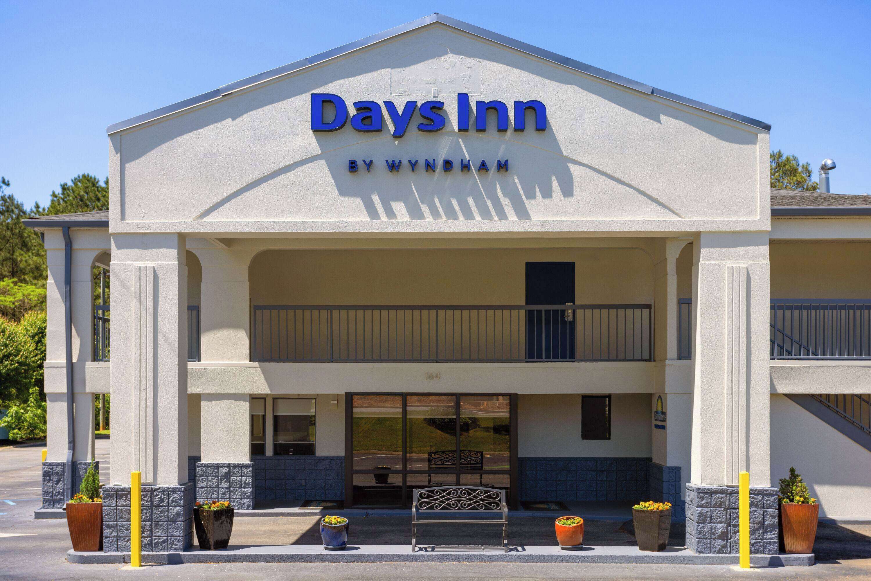 Ein Days Inn by Wyndham Gebäude mit Balkon, großen Fenstern und Pflanzkübeln.