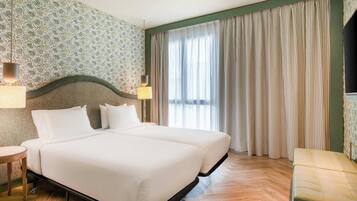 A double bed with a wooden frame, two bedside lamps, and a large window with curtains.