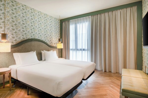 Una cama doble con estructura de madera, dos lámparas de noche y un ventanal con cortinas.