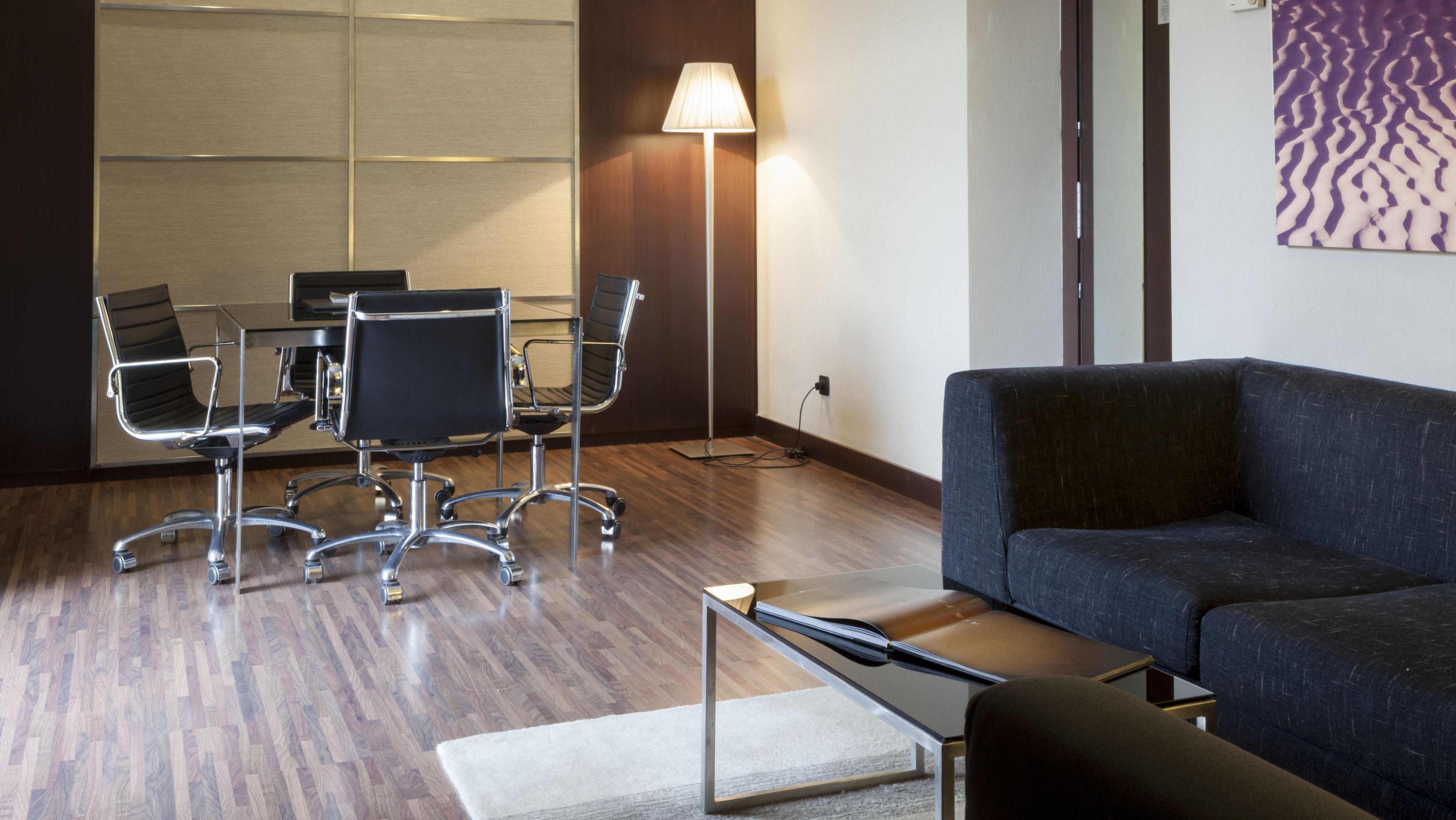 A modern conference room with a glass table, black office chairs, and a standing lamp.