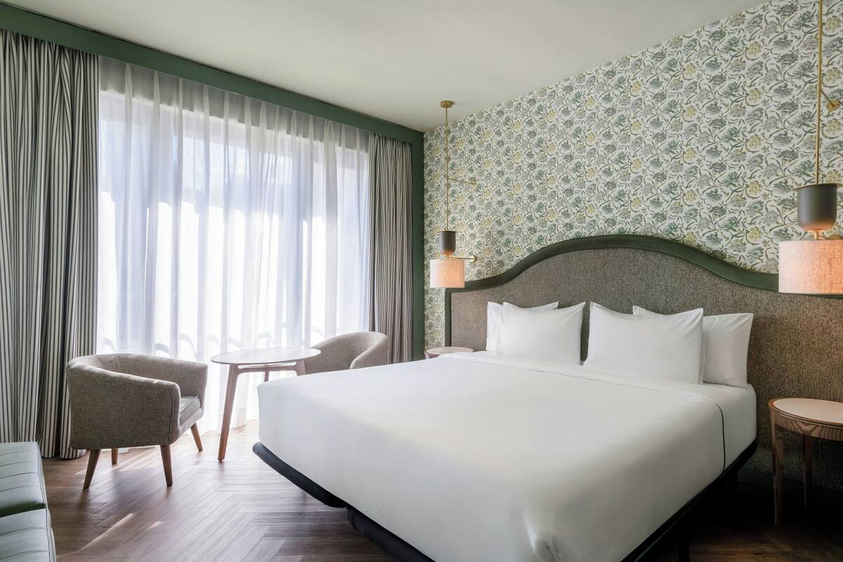 Een hotelkamer met een groot bed, twee stoelen, een klein tafeltje en een decoratieve wand.