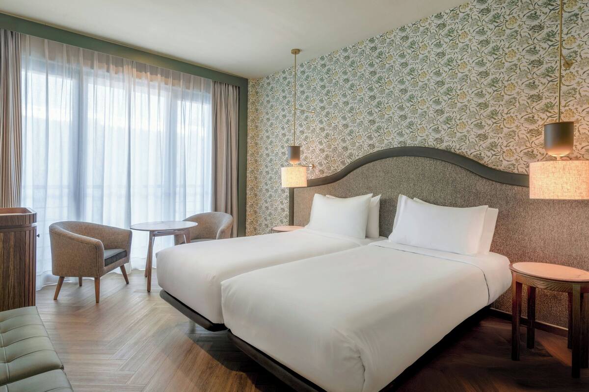 Een hotelkamer met twee bedden, een tafeltje, een stoel en een bureau.