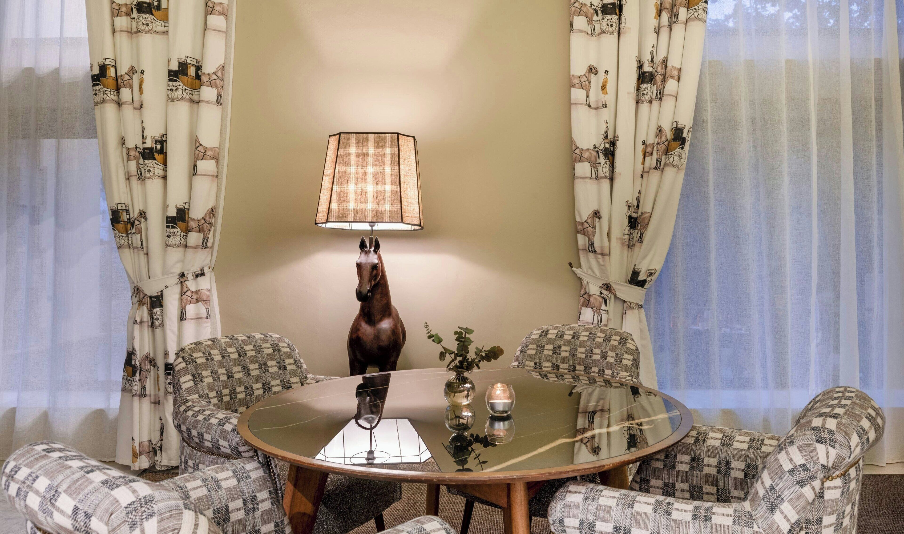Un coin repas comprenant une table ronde en verre, quatre chaises à motifs, une statue équestre décorative et une lampe de table.