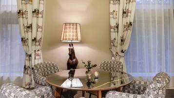Un coin repas comprenant une table ronde en verre, quatre chaises à motifs, une statue équestre décorative et une lampe de table.