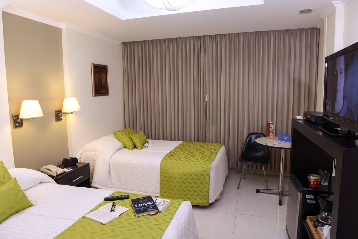 A hotel room with two beds, a desk with a chair, a television, and a minibar.